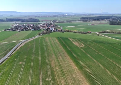 Luftaufnahme: grüne Felder, Dorf, sich kreuzende Straßen, Ackerland, klarer Tag.