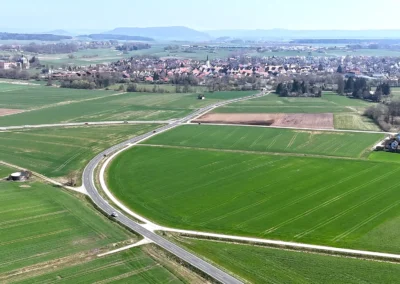 Luftaufnahme: grüne Felder, Straßen, kleine Stadt, entfernte Hügel, klarer Himmel.