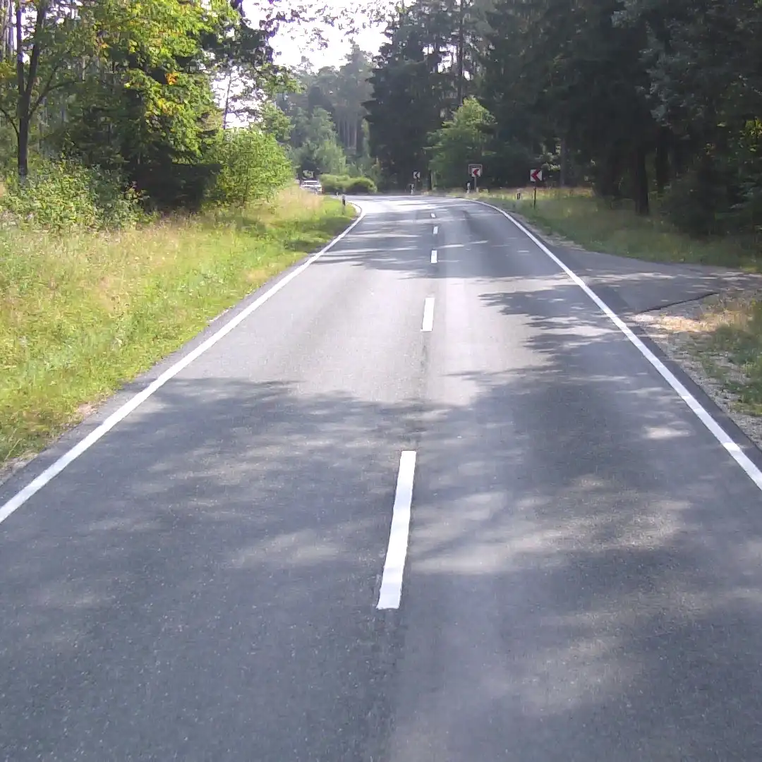 Kurvenreiche zweispurige Straße mit weißen Markierungen, Bäumen und Grünanlagen auf beiden Seiten. Kurvenreiche zweispurige Straße mit weißen Markierungen, Bäumen und Grünanlagen auf beiden Seiten.
