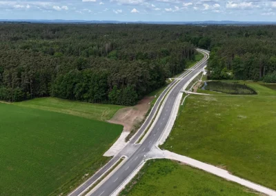 Luftaufnahme: Eine asphaltierte Straße schlängelt sich durch grüne Felder und Wälder bei Reckenstetten.