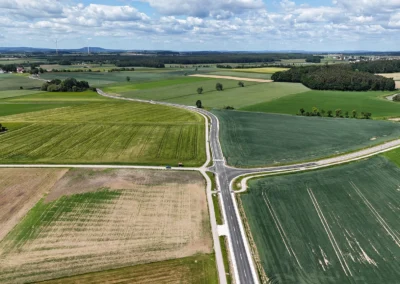 Luftaufnahme: ländliche Kreuzung, Ackerland, Bäume, teilweise bewölkter Himmel, neuer Straßenbau.