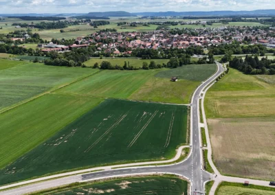 Luftaufnahme von sich kreuzenden Straßen, grünen Feldern, Kleinstadt, bewölktem Himmel.